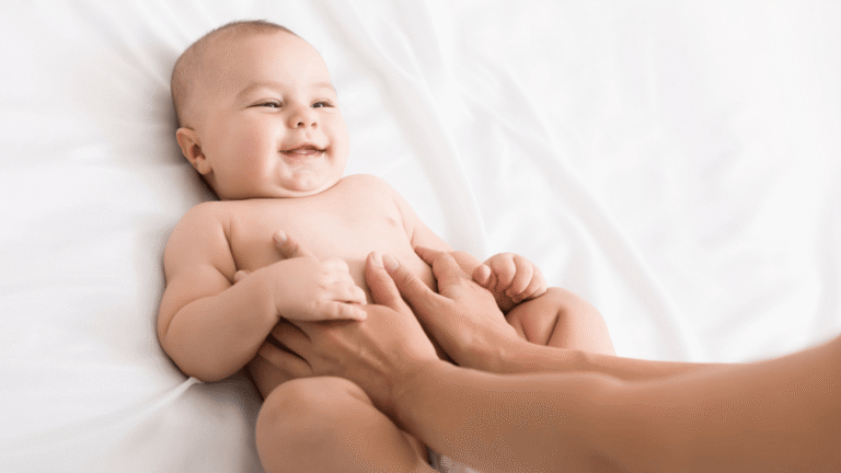 Baby smiling as hands gently touch her tummy during a moment of care.