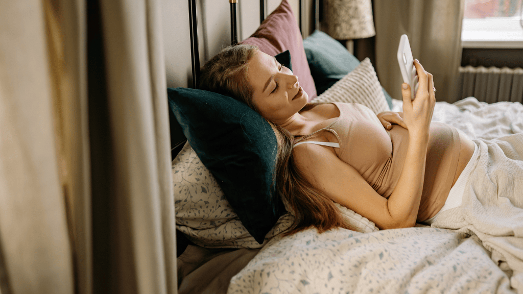 pregnant woman in the first trimester looking at her cell phone while resting in bed