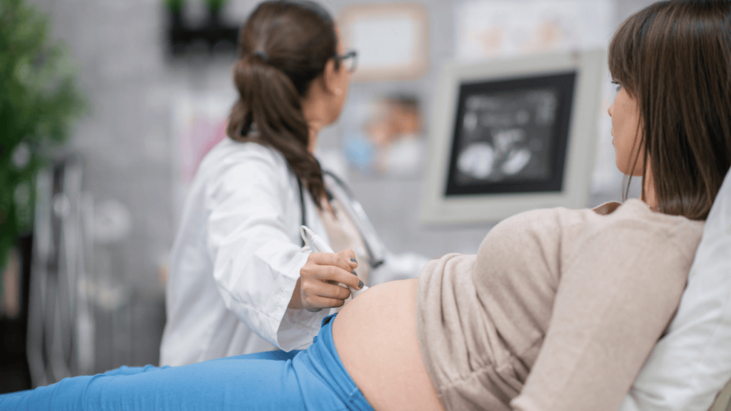 schwangere Frau in der Praxis eines Geburtshelfers, die während der Schwangerschaftsüberwachung eine Ultraschalluntersuchung betrachtet